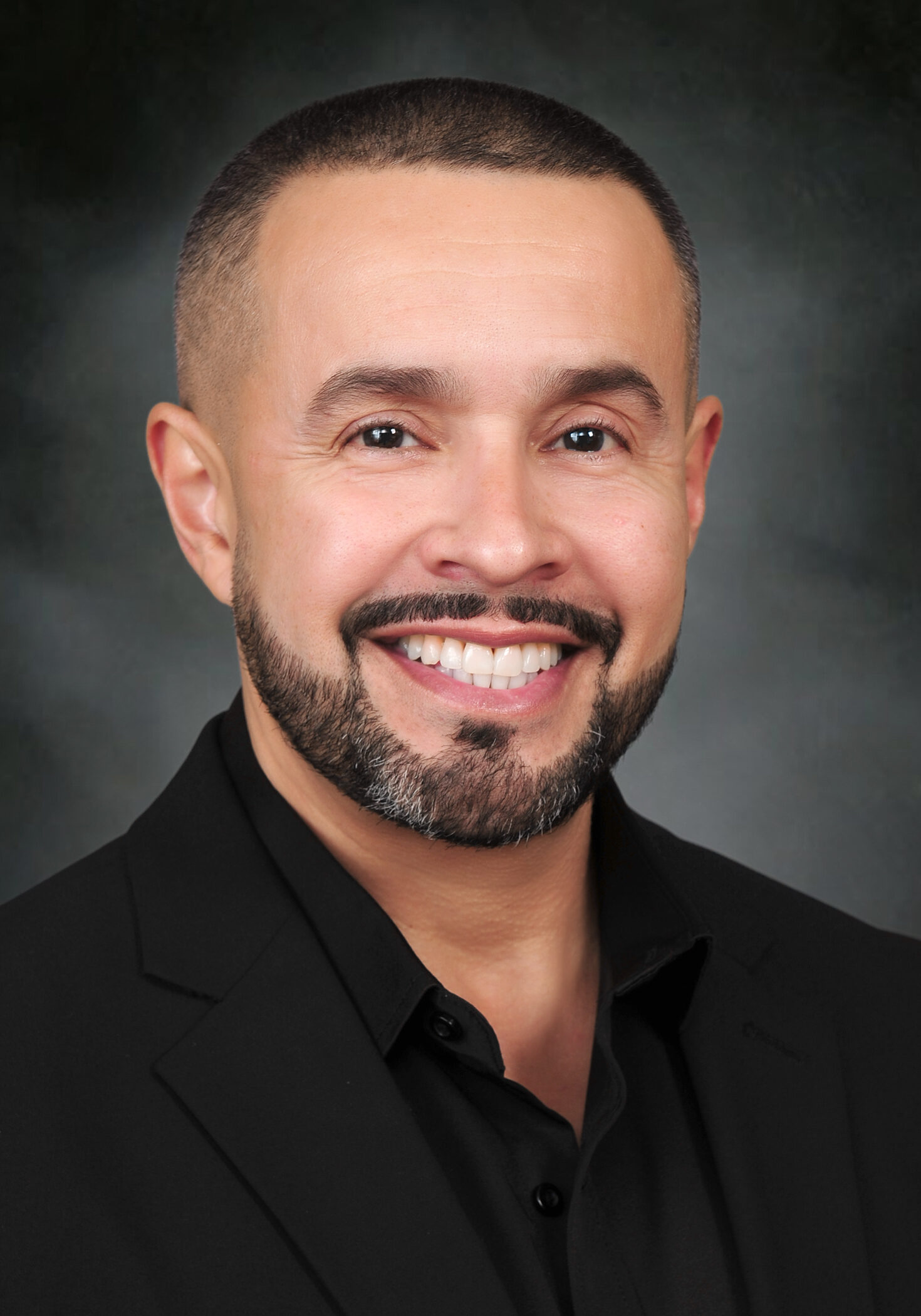 A man with a beard and mustache wearing a black suit.